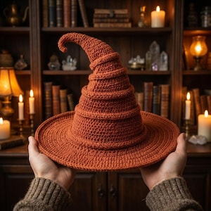 May include: A burnt orange crochet witch hat with a wide, flat brim and a tall, pointed, slightly curved crown. The hat is constructed from a textured yarn with visible stitch patterns, featuring a spiraling, ribbed design throughout the cone.