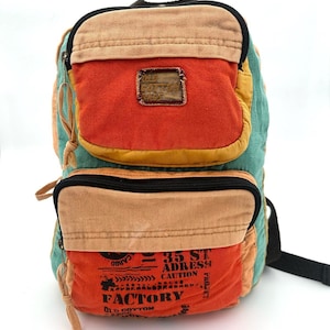 May include: A colorful backpack with multiple compartments. The backpack features a combination of orange, tan, and teal panels. The front pocket has the text "FACTORY" and "OLD COTTON". The backpack has black zippers and straps.