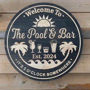 May include: A round wooden sign with the words "Welcome To The Pool & Bar" and "It's 5 O'Clock Somewhere" carved into it. The sign features a sun, palm trees, and drink illustrations. The year "2024" is also carved into the sign.