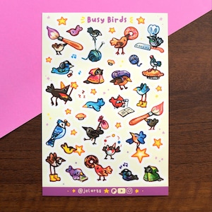 May include: A sticker sheet titled Busy Birds featuring various colorful cartoon birds engaged in activities like painting, reading, cooking, and wearing hats. The sheet includes small yellow stars and the text @jelarts at the bottom.