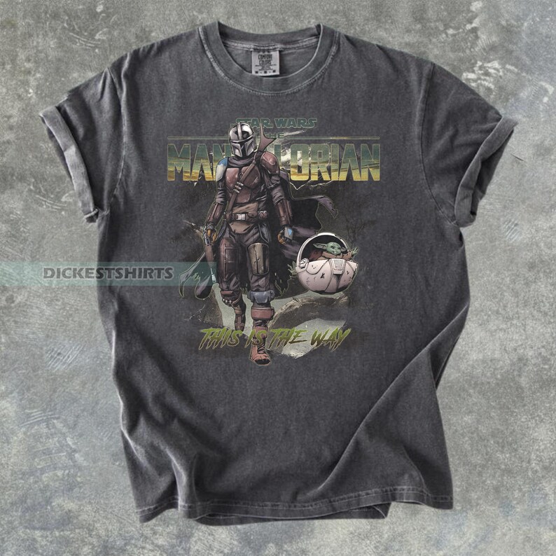 May include: Dark gray t-shirt featuring a Star Wars Mandalorian graphic. The design includes the Mandalorian character, Grogu, and the text "This is the Way." The shirt has a vintage, distressed look.