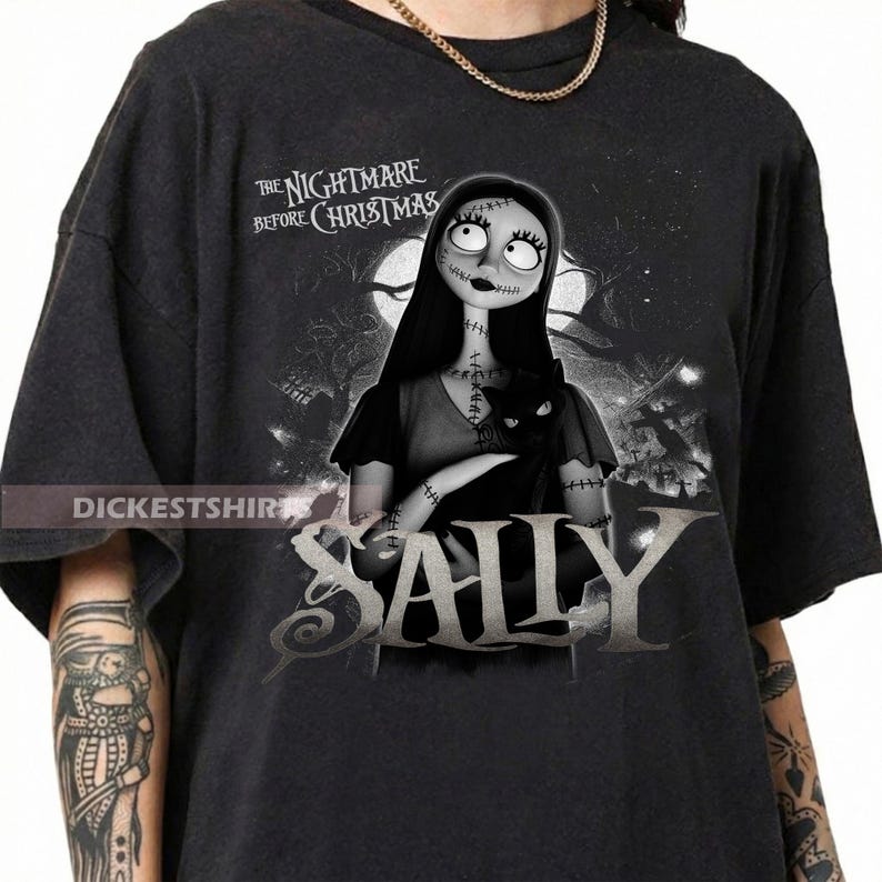 May include: Dark gray t-shirt featuring Sally from "The Nightmare Before Christmas." The design includes Sally holding a black cat, with the movie title above and her name in large letters below. The shirt has a distressed look.