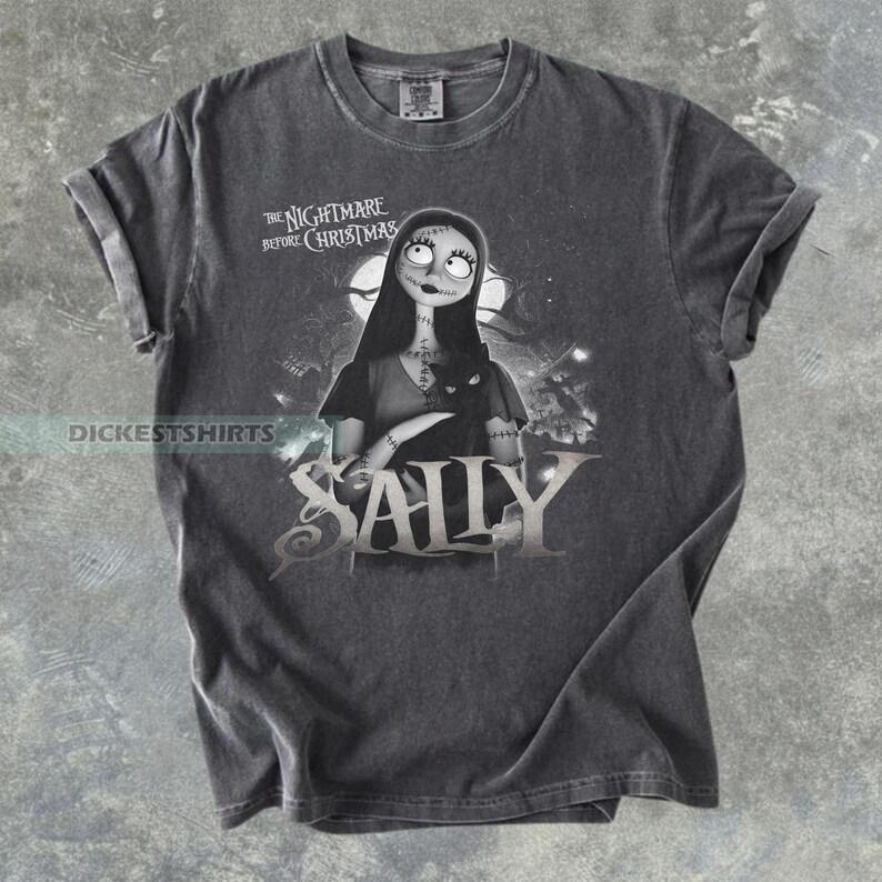 May include: Dark gray t-shirt featuring Sally from "The Nightmare Before Christmas." The graphic shows Sally with a black cat, the movie title, and the character's name. The shirt has rolled-up sleeves and a crew neck.