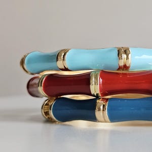 May include: Stack of three colorful bangles. The bangles are blue, red, and navy blue with gold-colored accents. The bangles are stacked on top of each other, with the blue bangle on top, the red in the middle, and the navy blue on the bottom.