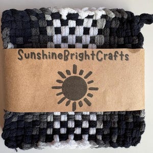 May include: A woven hot pad in a checkerboard pattern of black, white, and gray. A brown paper band wrapped around the pad features the text "SunshineBrightCrafts" and a sun graphic.