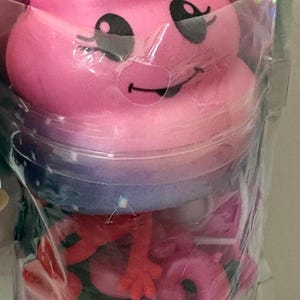 May include: A pink squishy toy shaped like a smiling swirl with black eyes and a mouth, packaged in a clear plastic bag containing various small red and pink plastic animal figures and colorful confetti pieces visible through the transparent material.