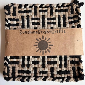 May include: A woven potholder with a geometric pattern in black, tan, and cream colors. A brown paper band with the text "SunshineBrightCrafts" and a sun graphic is wrapped around the potholder.