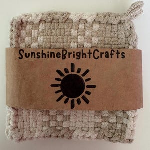 May include: A square, woven cotton potholder in alternating shades of beige and cream, featuring a small corner loop. A brown paper band wraps around the center, printed with the text SunshineBrightCrafts and a black sun icon graphic.