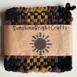 May include: A woven square hot pad in black, brown, and gold. A brown paper band with the text "SunshineBrightCrafts" and a sun graphic wraps around the pad. A loop is attached for hanging.