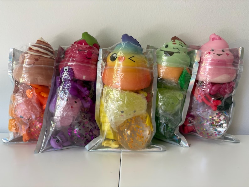May include: Five clear plastic pouches each containing a colorful squishy toy shaped like a swirl of soft serve ice cream with a smiling face, accompanied by smaller assorted sensory toys including glittery balls and small animal figures.