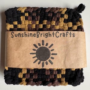 May include: A woven potholder in black, brown, and gold. A brown paper band with the text "SunshineBrightCrafts" and a sun graphic wraps around the potholder.