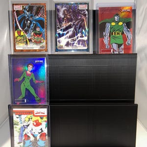 May include: A black display stand holding several Marvel trading cards. The cards feature characters like Grim Reaper, Storm, and Doctor Doom. The cards are in protective cases, with some labeled "2023 Marvel Platinum".