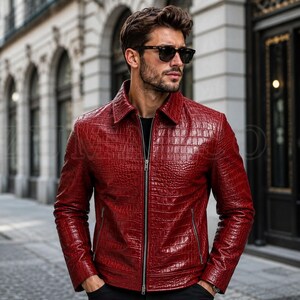 Puede incluir: Una chaqueta de color rojo intenso con un patrón texturizado de piel de cocodrilo, cuello clásico y cierre de cremallera metálica plateada. La prenda incluye dos bolsillos laterales con cremalleras y mangas largas con puños.