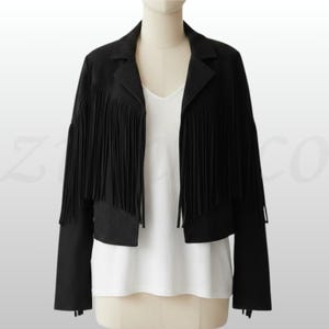 May include: A black suede jacket with fringe detailing. The jacket has a classic collar and long sleeves. The fringe is along the front and sleeves of the jacket. The jacket is displayed on a mannequin over a white top.