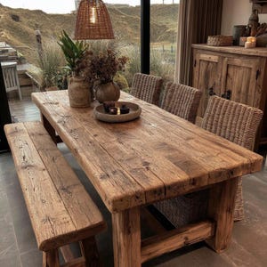 May include: A rectangular dining table made of reclaimed wood with a thick, weathered surface and sturdy legs, accompanied by a matching wooden bench and three woven wicker chairs, featuring a round tray with small bowls on the tabletop.