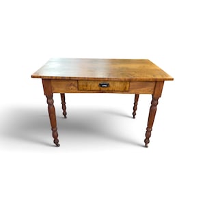 May include: A rectangular wooden table with a natural brown grain finish, featuring a single central drawer with a dark metal pull handle. The table is supported by four turned legs, each equipped with small metal casters at the base.