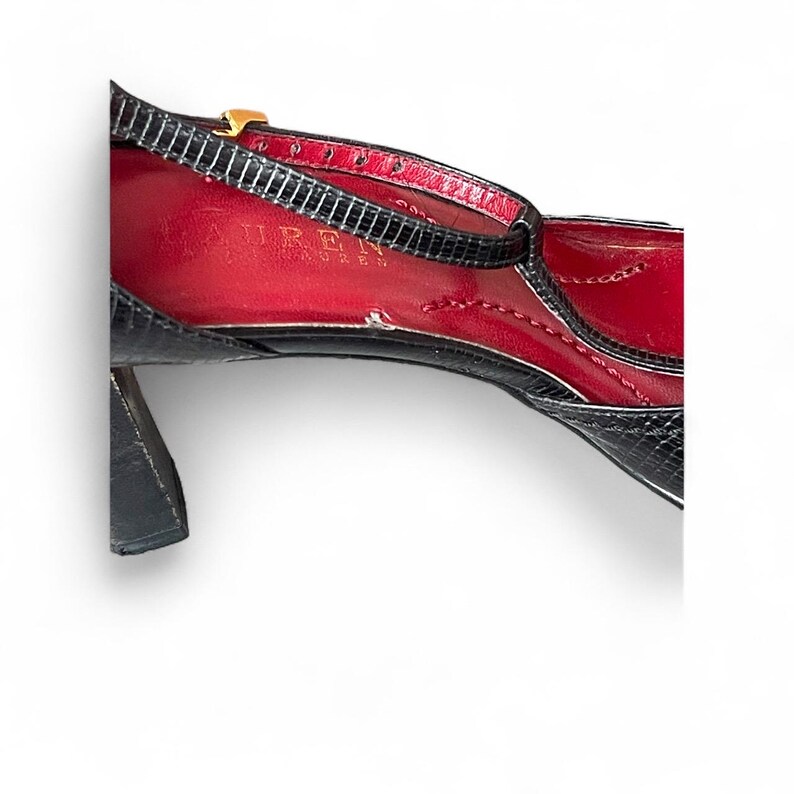 May include: Black and red high-heeled shoe with a strap and gold buckle. The shoe has a textured black exterior and a red interior. The heel is approximately 3 inches.