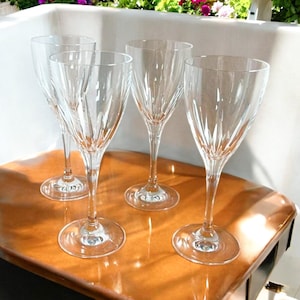 Może przedstawiać: Cztery przezroczyste szklane kieliszki do wina z wzorem z cięcia szkła. Kieliszki są ułożone na drewnianej powierzchni.