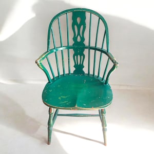 May include: A green wooden chair with a spindle back and a carved design on the back. The chair has a distressed finish and is in good condition.