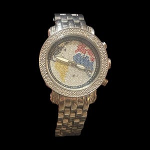 May include: A silver-toned wristwatch with a world map design on the face. The map features colorful accents, including red, blue, and yellow. The watch has a diamond-studded bezel and band.