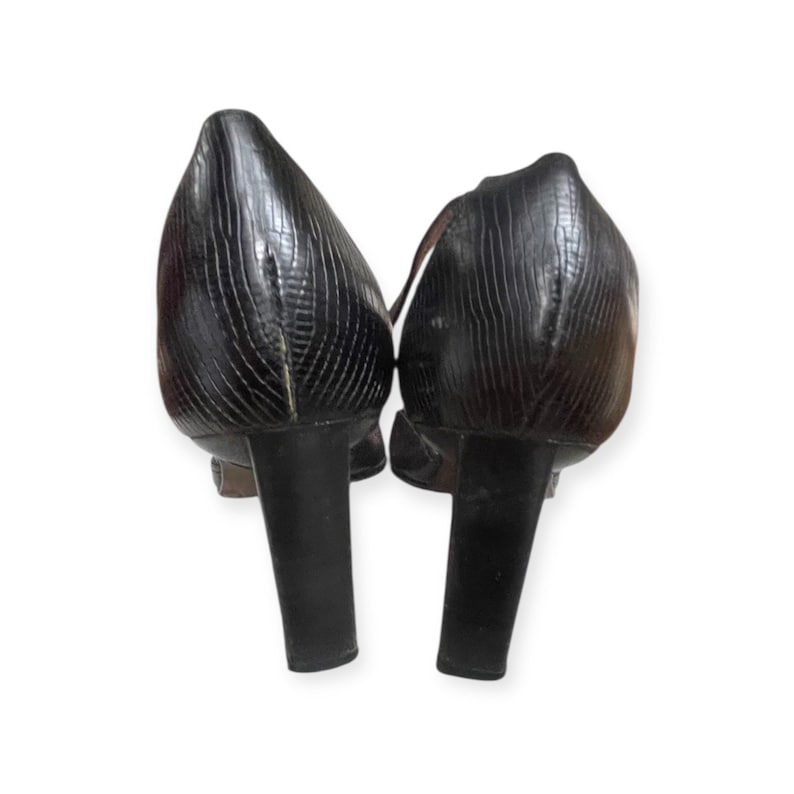 May include: A pair of black, textured high-heeled shoes. The heels are thick and cylindrical. The shoes have a pointed toe and a strap across the top of the foot.