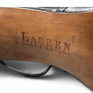 May include: Close-up of the sole of a black high-heeled shoe. The brand name "LAUREN RALPH LAUREN" is stamped in dark ink on the brown sole. The shoe size is 10M.