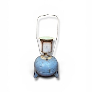 Peut inclure: Lampe lanterne vintage bleue et argentée avec une base ronde et une poignée. La lanterne a un dessus cylindrique avec une étiquette et un couvercle vert. La lanterne est ancienne, avec des signes d'usure.