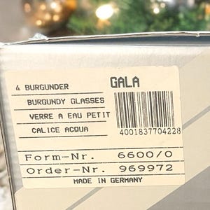 Może przedstawiać: Białe pudełko z etykietą, na kt&oacute;rej widnieje napis "GALA" i "BURGUNDY GLASSES". Etykieta zawiera r&oacute;wnież tekst "VERRE A EAU PETIT", "CALICE ACQUA", "Form-Nr. 6600/0", "Order-Nr. 969972" i "MADE IN GERMANY".