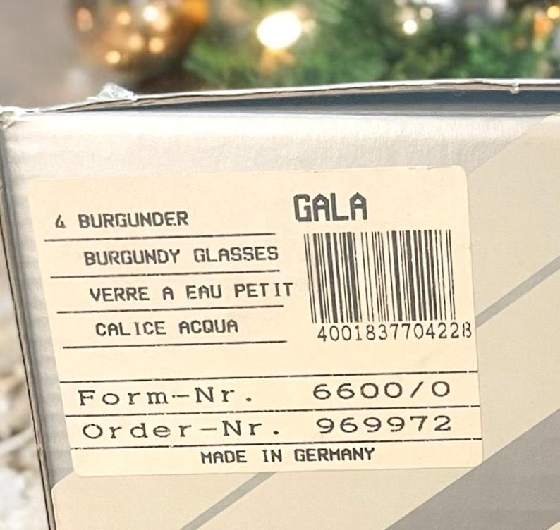 Może przedstawiać: Białe pudełko z etykietą, na kt&oacute;rej widnieje napis "GALA" i "BURGUNDY GLASSES". Etykieta zawiera r&oacute;wnież tekst "VERRE A EAU PETIT", "CALICE ACQUA", "Form-Nr. 6600/0", "Order-Nr. 969972" i "MADE IN GERMANY".