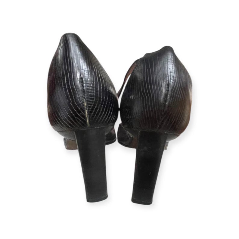 May include: A pair of black, textured high-heeled shoes. The heels are thick and cylindrical. The shoes have a pointed toe and a strap across the top of the foot.
