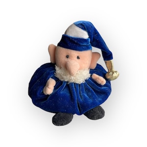 Puede incluir: Muñeco de gnomo de peluche con un atuendo de terciopelo azul, barba blanca y gorro puntiagudo. El gorro tiene una parte superior blanca y una borla dorada. La muñeca tiene una cara rosada, orejas grandes y zapatos negros.