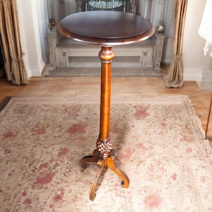 May include: A dark brown wooden pedestal table with a round top and three legs. The table is standing on a patterned rug.