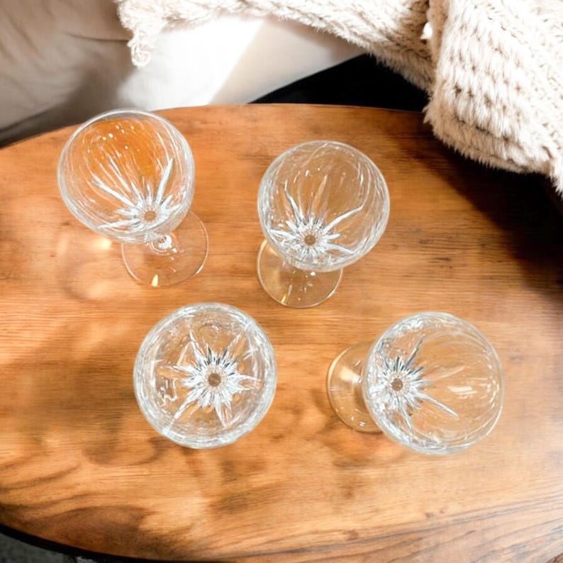 Może przedstawiać: Cztery przezroczyste szklane kieliszki do wina z wyciętym wzorem z kryształu stoją na drewnianej powierzchni.