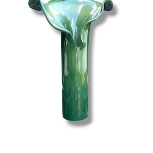 Può includere: Un vaso alto di vetro verde con una parte superiore svasata a forma di petalo. Il vaso ha un corpo cilindrico e una finitura lucida. La parte superiore del vaso ha una tonalità verde più chiara, creando un effetto sfumato. È un oggetto decorativo.