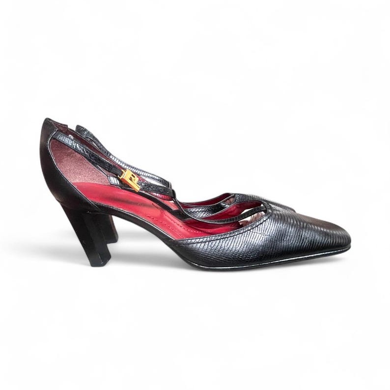May include: Black high-heeled shoes with a textured finish. The shoes have a pointed toe, a strap across the foot, and a strap around the ankle. The interior is red, and the heel is a solid black block. The shoes have a gold-colored buckle.