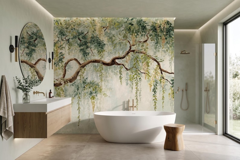 May include: A bathroom featuring a large wall mural of a sprawling tree with hanging green leaves and yellow flowers. The room includes a white oval freestanding bathtub, a wooden vanity with a white sink, a round mirror, and a small wooden stool.