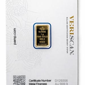 Puede incluir: Un lingote de oro fino de 1g con pureza 999.9, encapsulado en una tarjeta de ensayo blanca PAMP Suisse. La tarjeta muestra el texto PAMP, VERISCAN y detalles como el n&uacute;mero de certificado D129356, pureza Au 999.9, peso 1g y firma del ensayador.