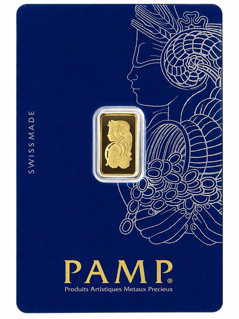Puede incluir: Un lingote de oro rectangular encapsulado en una tarjeta protectora azul. El lingote presenta un relieve de una mujer con un cuerno de la abundancia. La tarjeta muestra el texto SWISS MADE, PAMP y Produits Artistiques Metaux Precieux.