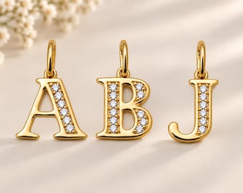 Puede incluir: Tres colgantes de letras en oro con las letras A, B y J. Cada colgante tiene un acabado en oro pulido y está decorado con una fila vertical de pequeñas piedras transparentes de corte redondo incrustadas en la parte frontal de las letras.