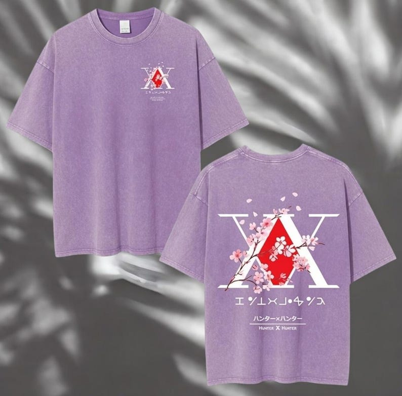 May include: A lilac-colored t-shirt featuring a graphic design on the front and back. The front design includes a red and white emblem with Japanese text. The back design features a large white "X" with a red diamond and cherry blossom accents.