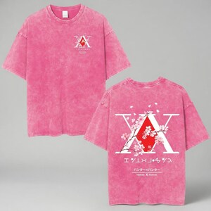 May include: Pink t-shirt with a distressed wash effect. The front features a white and red graphic. The back displays a large white "X" with a red center, cherry blossom branches, and Japanese text. The shirt is short-sleeved.