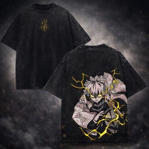 Pode incluir: Camiseta preta com um emblema dourado na frente e um gráfico de um personagem de anime com raios amarelos nas costas. A camiseta tem uma aparência vintage lavada.