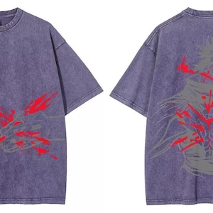 May include: A purple t-shirt with short sleeves, featuring a graphic on the front and back. The front has a red and grey abstract design. The back displays a similar design in red and grey, depicting a figure.