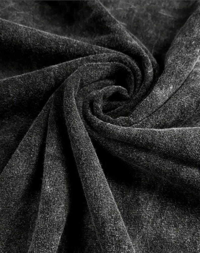 May include: Close-up of a dark gray fabric with a textured surface. The fabric is draped and folded, creating shadows and highlights. The material appears to be soft and possibly woven, with a subtle pattern visible.