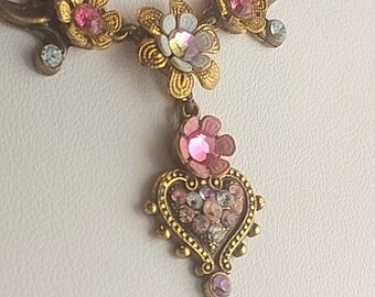 May include: A gold necklace with a heart pendant and floral accents. The heart pendant is adorned with pink and clear crystals. The necklace features a delicate chain and a floral design with pink and white crystals.