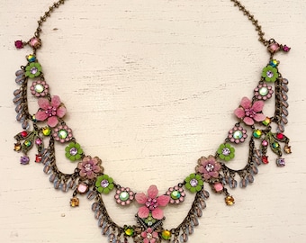 May include: A decorative necklace with a bronze chain and pendant. The pendant features pink flowers, green leaves, and colourful gemstones. The necklace has a delicate, ornate design, with dangling crystal beads.