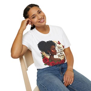 Op de afbeelding: Wit T-shirt met een afbeelding van een zwarte vrouw met een knot, rode rozen en vlinders. De tekst luidt "She is more precious than Rubies". Het T-shirt wordt door een persoon gedragen.