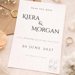 May include: A wedding invitation with the names Kiera & Morgan, and the date June 30, 2027. The invitation is on a cream-colored card with elegant typography. An envelope with a heart-shaped seal and a gold ring are also visible.