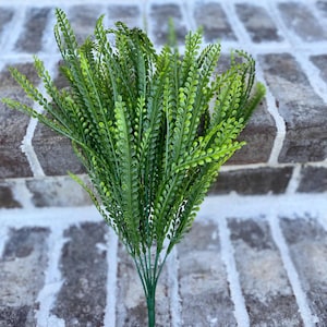 May include: A bundle of artificial greenery with vibrant green leaves. The leaves are small and closely spaced along the stems, creating a full, textured appearance. The stems are a darker green, and the overall effect is a fresh, natural look, suitable for home decor.