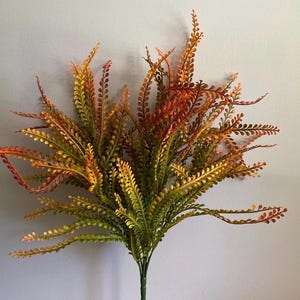 May include: A vibrant artificial plant with a mix of green, yellow, and orange leaves. The plant has a full, bushy appearance with many delicate, fern-like fronds. The stems are a deep green, and the overall effect is natural and colorful.